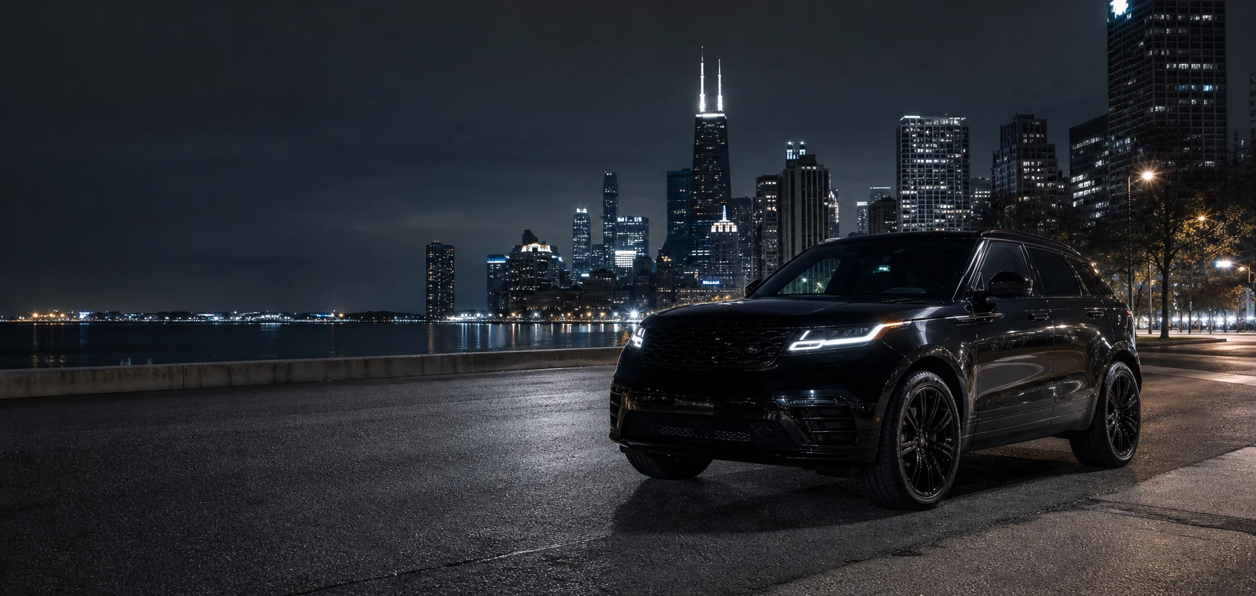 Dark polished vehicle in front of a Chicago skyline at night